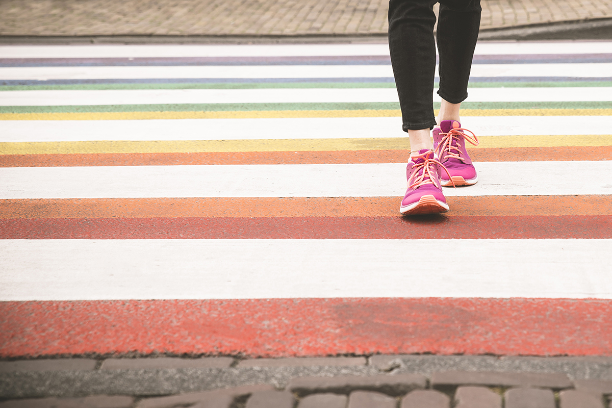 A person wearing pink sneakers and black trousers walks across a colourful crossing.