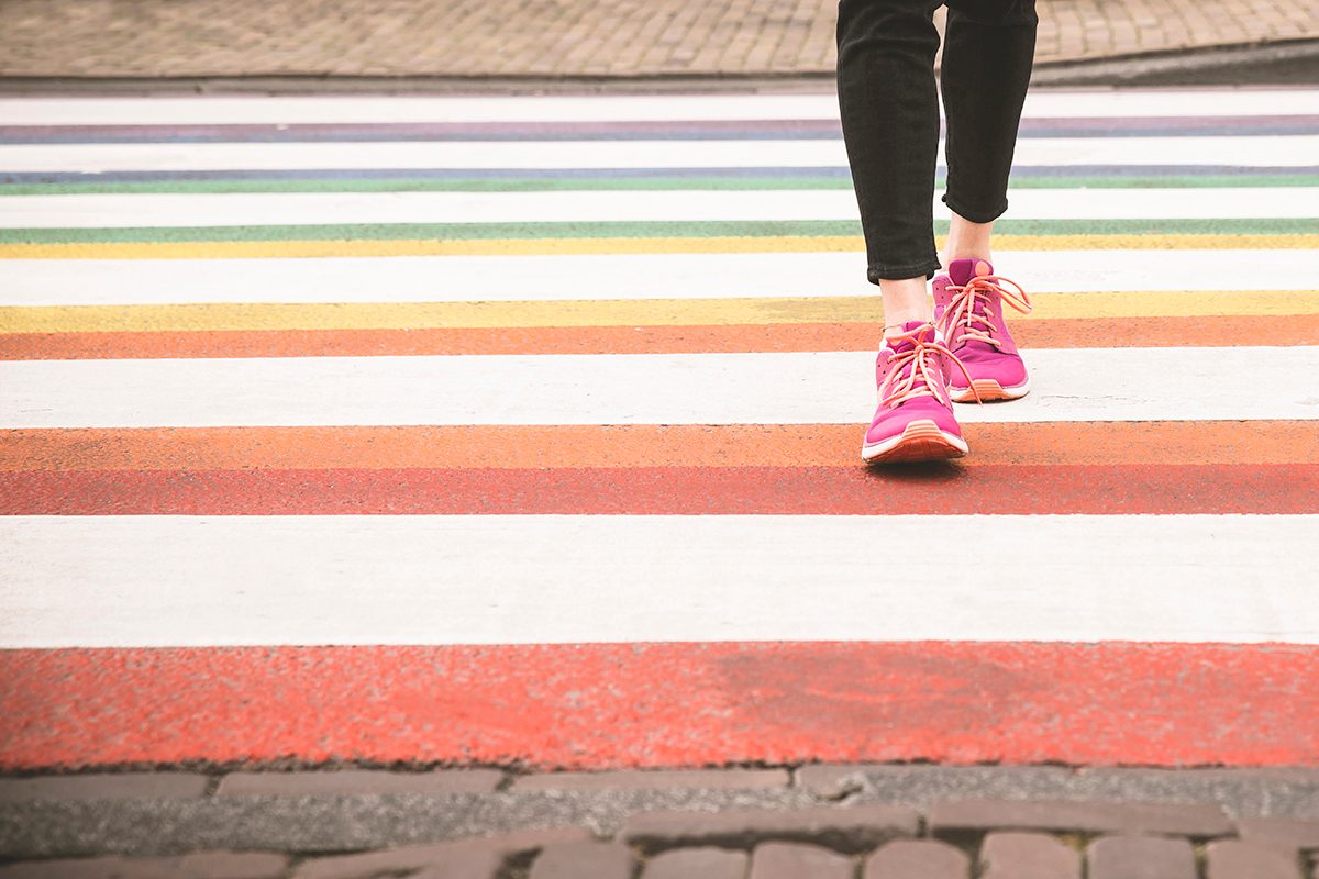 A person wearing pink sneakers and black trousers walks across a colourful crossing.