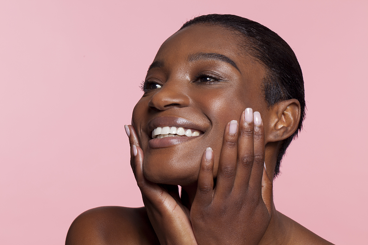 A smiling woman touching her face against a pink background