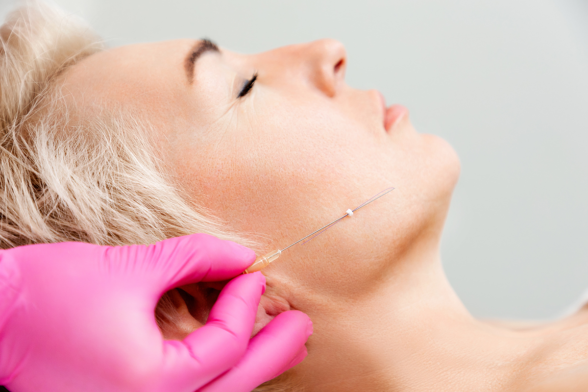 A hand wearing a pink latex glove holds a needle to a client's face