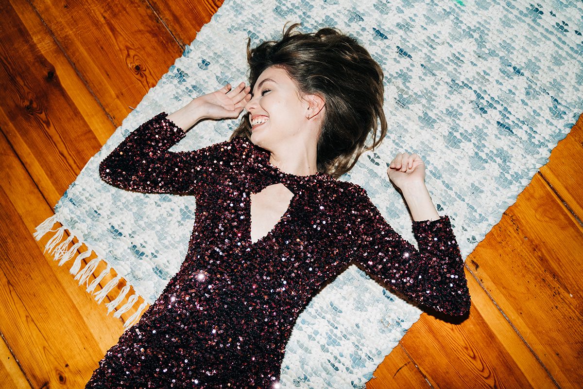 A woman wearing a sparkly dress is lying on a floor rug and smiling
