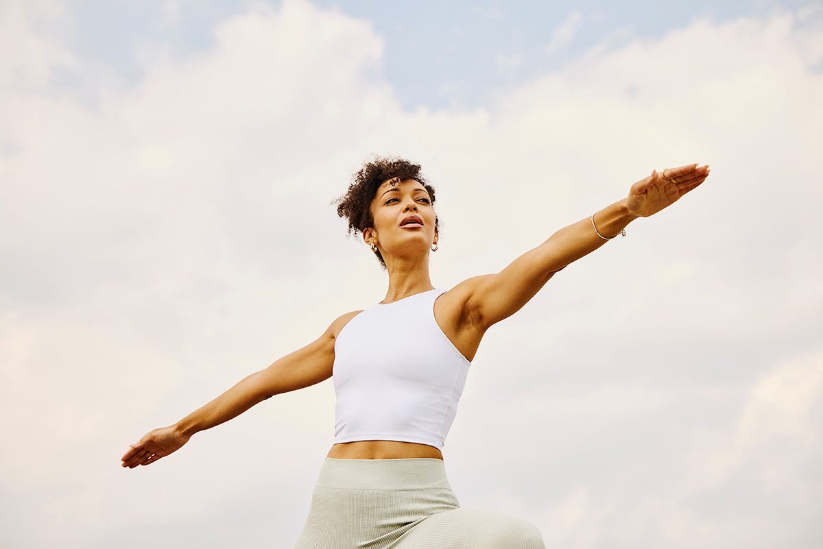 A woman stands in a warrior pose outdoors
