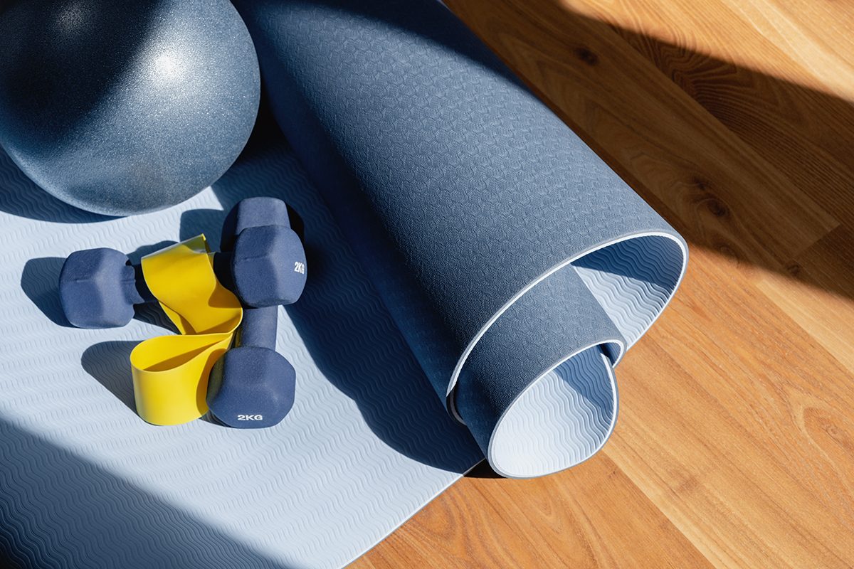 A pair of dumbbells, a resistance band and an exercise ball on a yoga mat