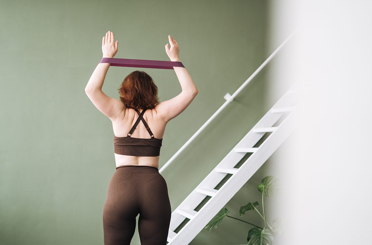 A woman performing an arm exercise with a resistance band in a green room