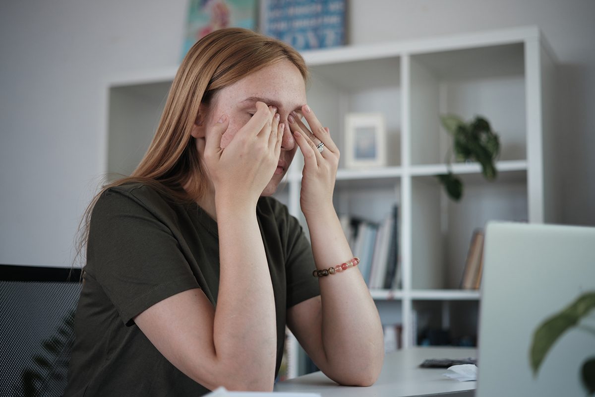 A woman is sitting at a desk rubbing her eyes