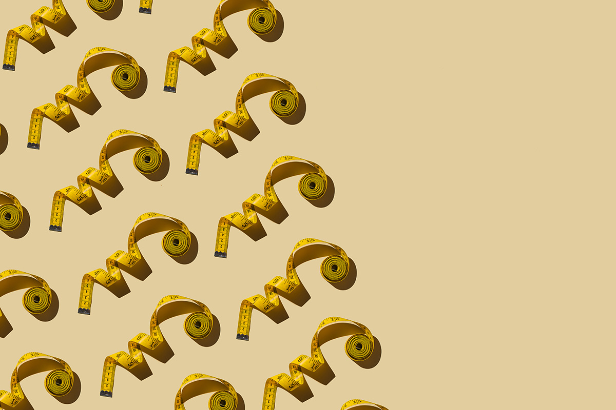 A pattern of yellow, coiled up measuring tapes is arranged diagonally on a beige background.