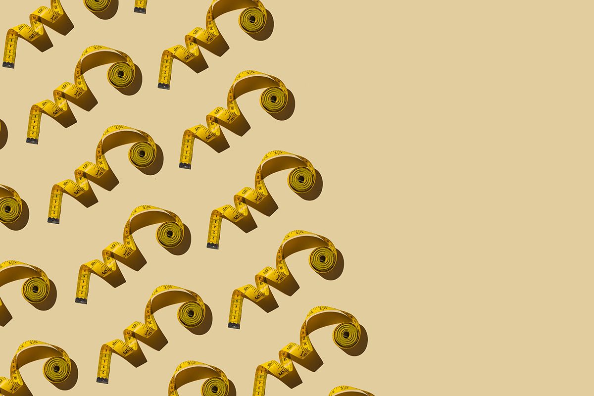 A pattern of yellow, coiled up measuring tapes is arranged diagonally on a beige background.