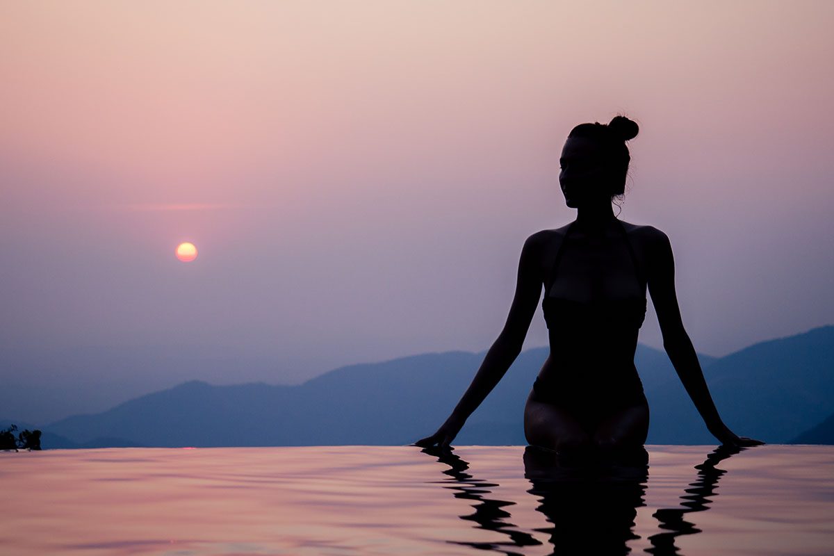 A woman standing in an infinity pool at sunset