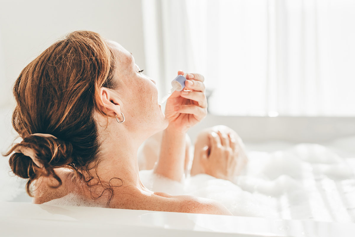 A woman applying skincare with a pipette in the bath