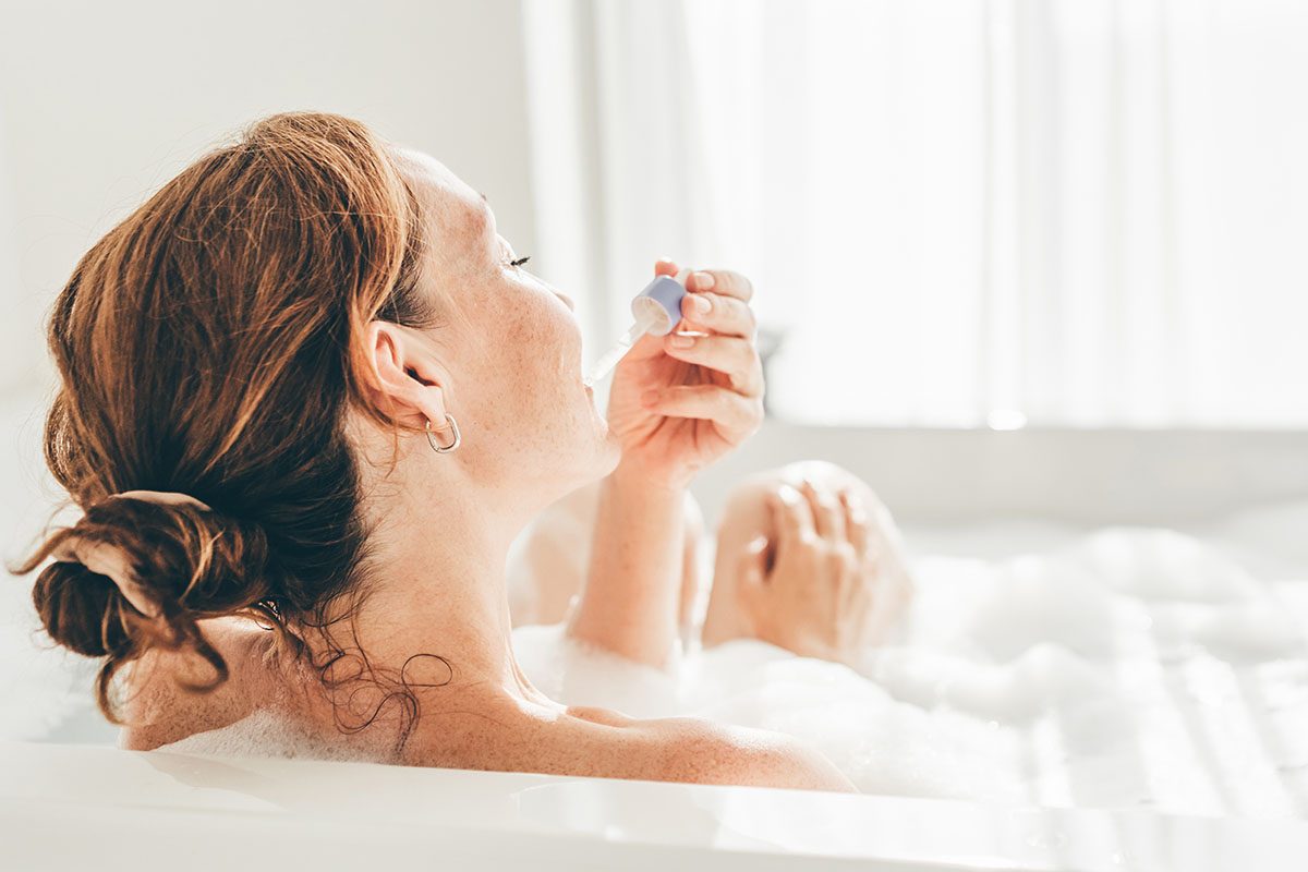 A woman applying skincare with a pipette in the bath