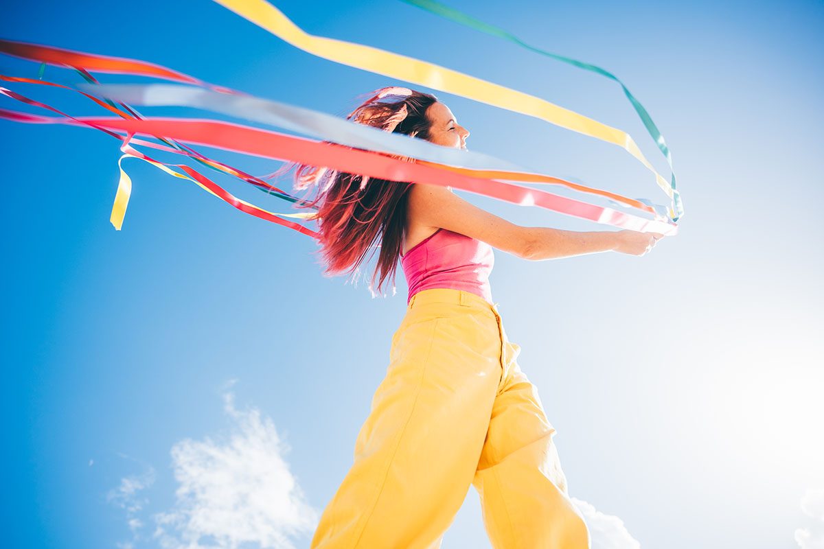 A woman walks with colourful ribbons in her hand against a blue sky