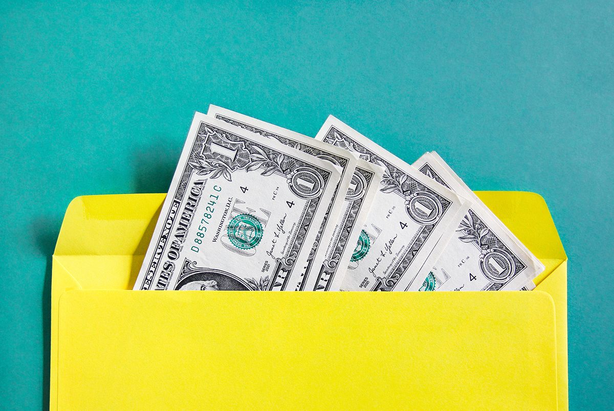 Dollar bills in a yellow envelope against a green background