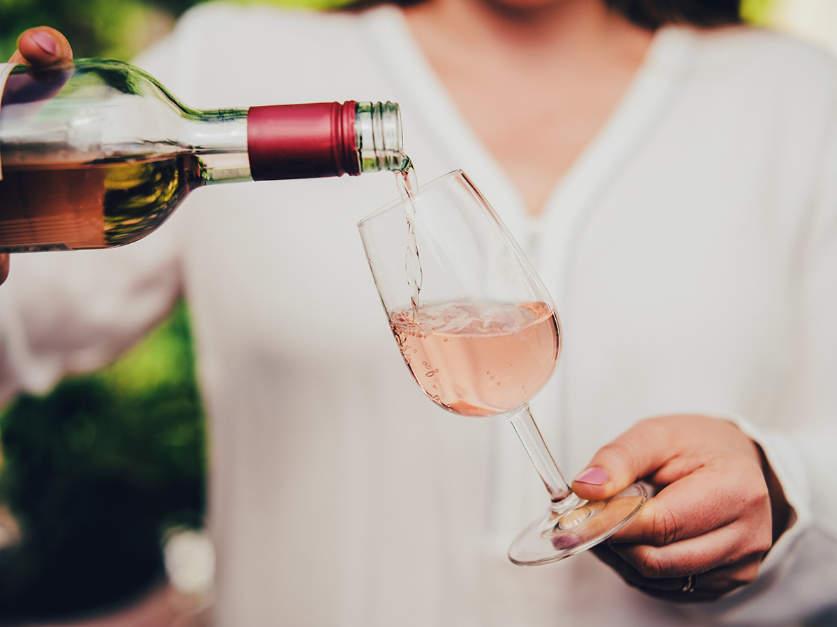 A woman is pouring rosé into a wine glass. 