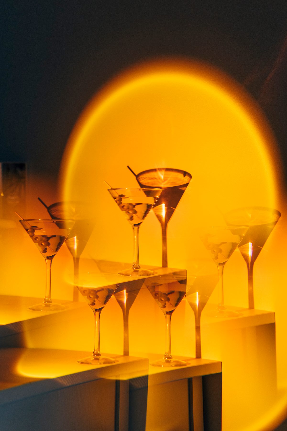 A warm orange light shines on a collection of martini cocktails