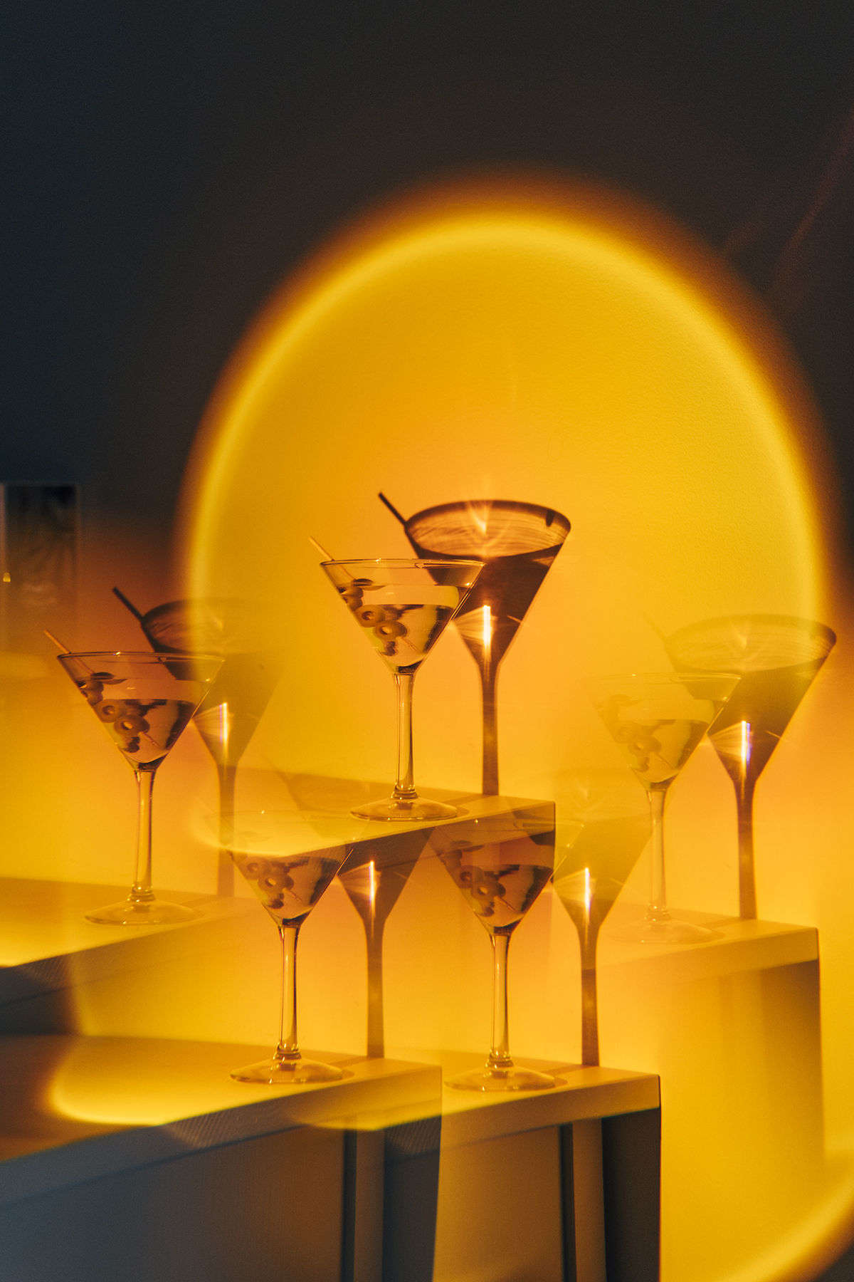 A warm orange light shines on a collection of martini cocktails