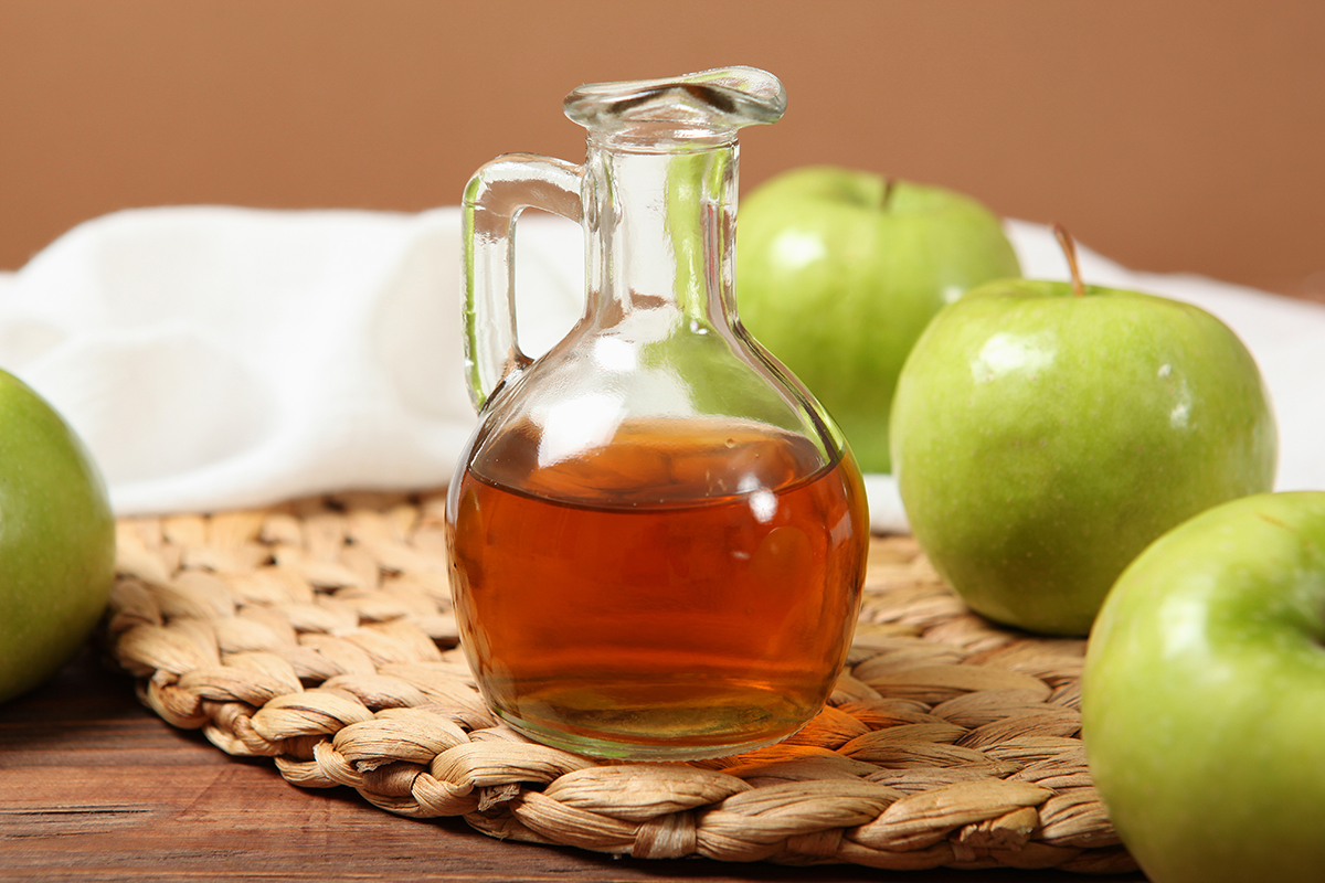 A glass bottle of apple cider vinegar beside green apples 