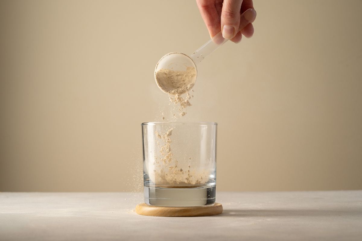 A hand tipping a spoonful of powder into a glass