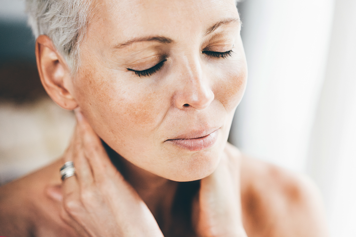 A woman touching her neck with her eyes closed