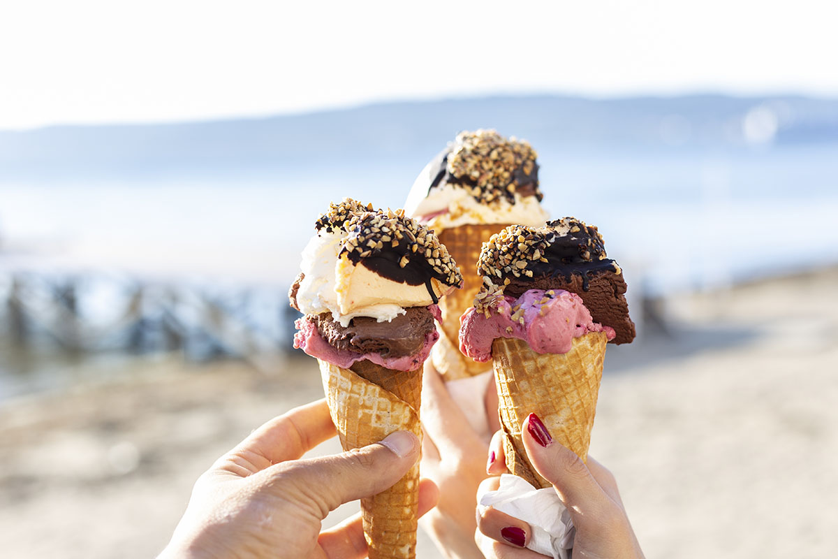 Three hands holding up ice cream cones against a blurred outdoor setting