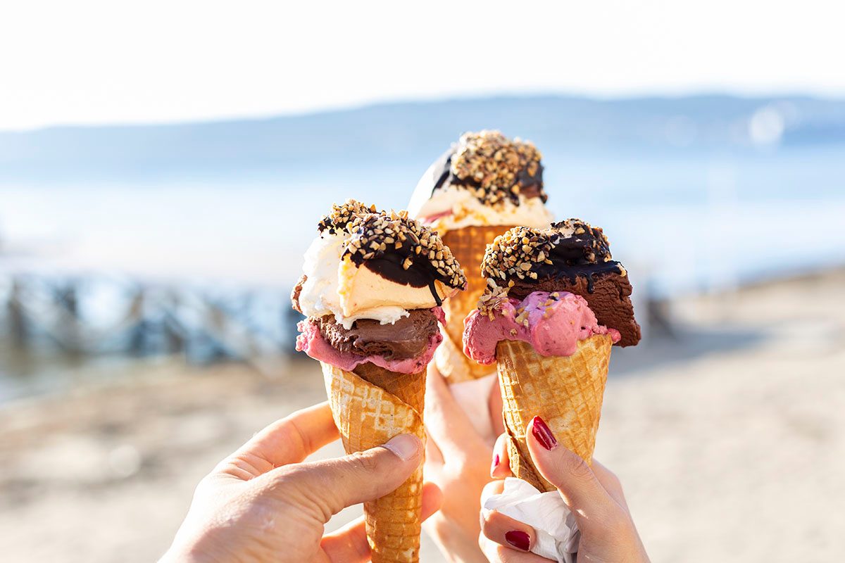 Three hands holding up ice cream cones against a blurred outdoor setting