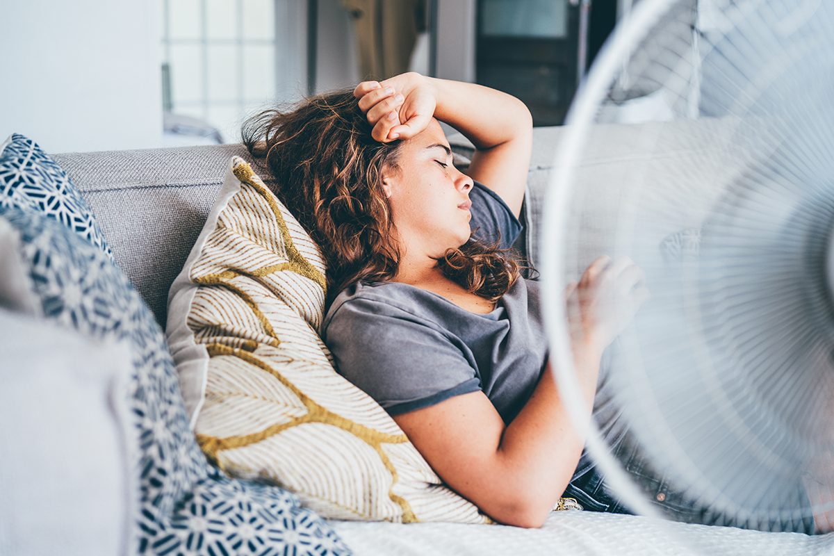 A woman lies on a sofa next to an electric fan