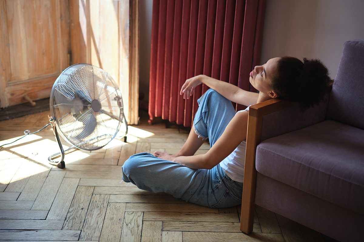 A woman is slumped against a sofa facing an electric fan
