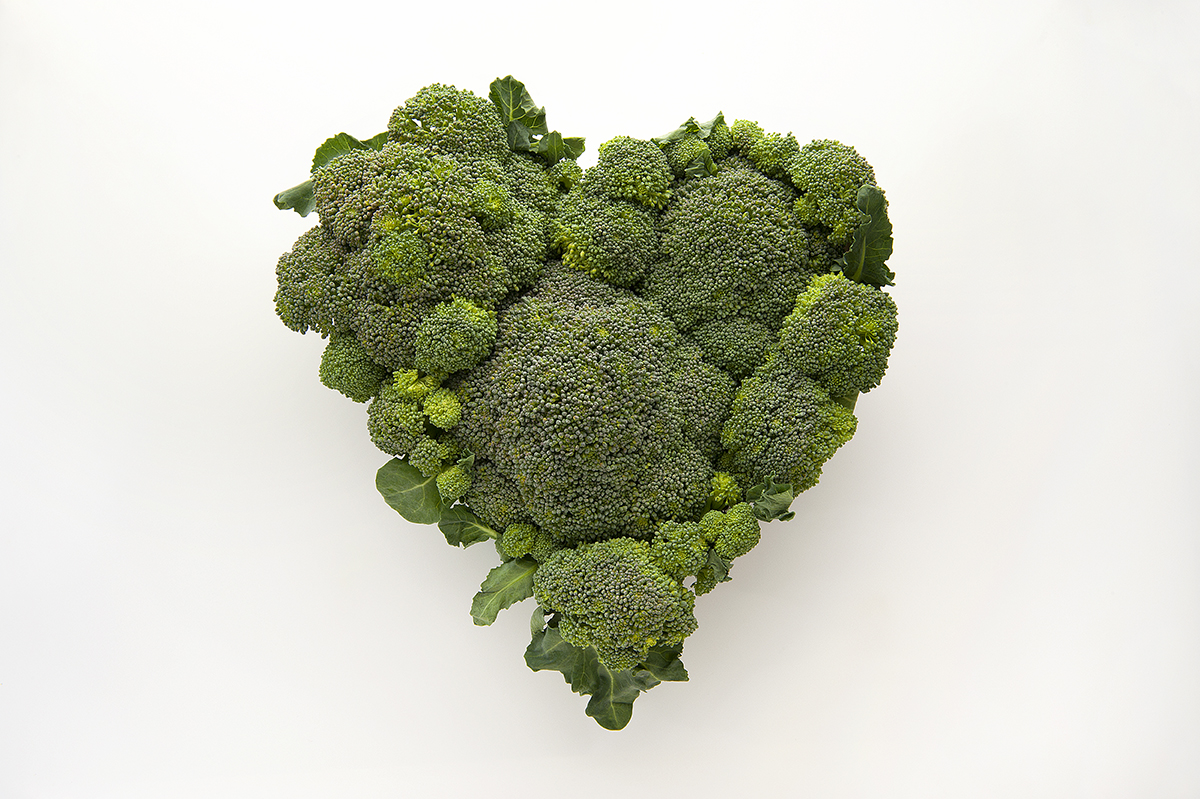 Broccoli florets are positioned in the shape of a heart against a white background.