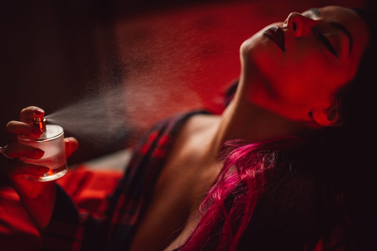 A woman spritzing herself with perfume in a red light