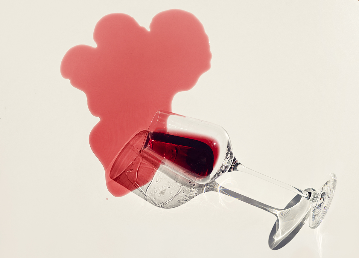 A wine glass lies on its side, spilling red wine onto a white background.