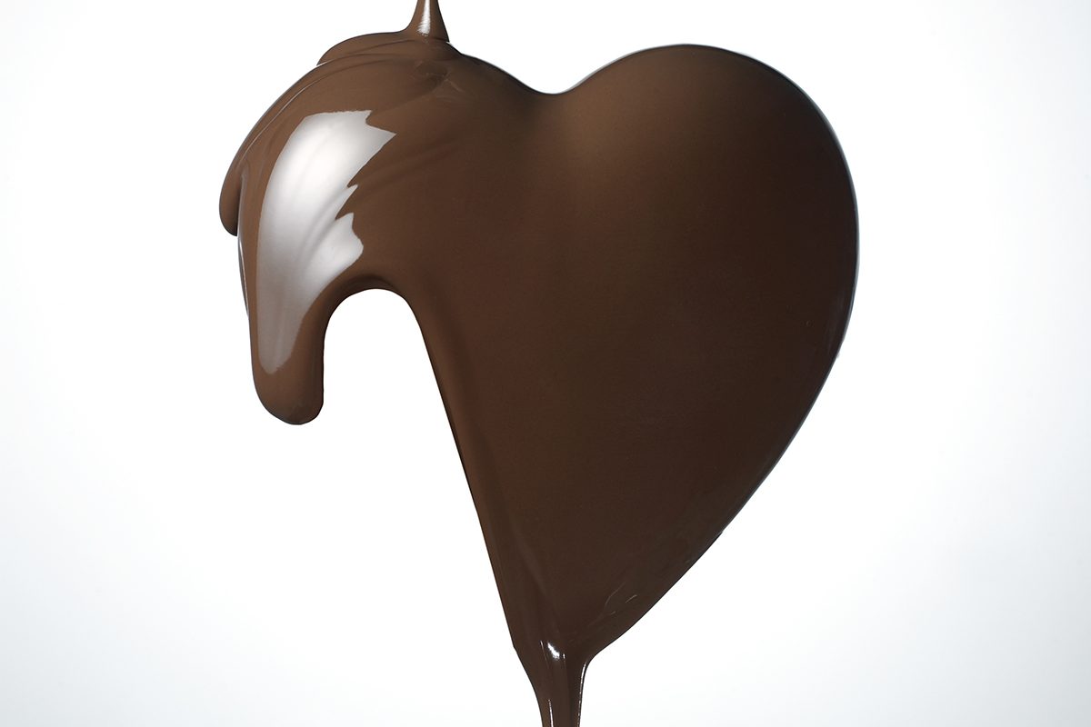 A stream of chocolate forms a heart shape against a white background.