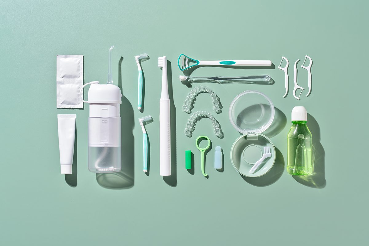 An assortment of dental items, including various tools, retainers, floss picks, a toothbrush and toothpaste, against a green background