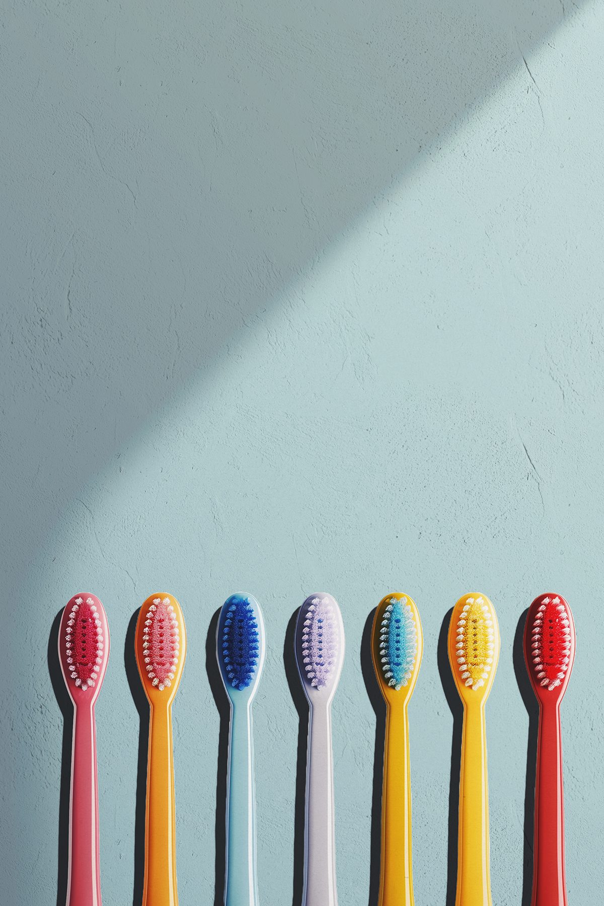 Colourful toothbrushes are arranged in a line against a green background