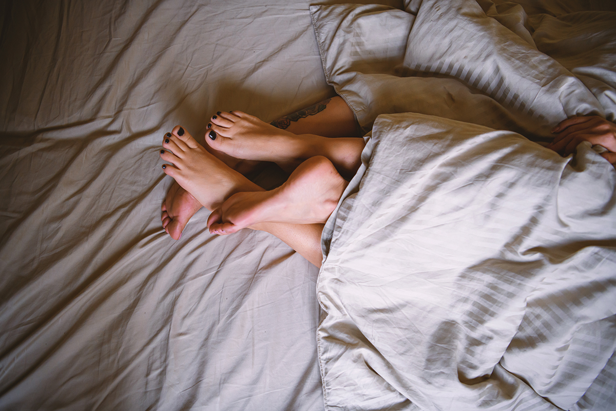 A couple’s bare feet poking out of a duvet