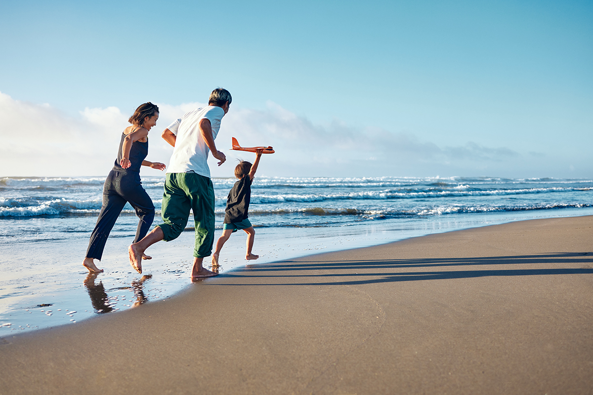 Two parents chasing their young son on a beach