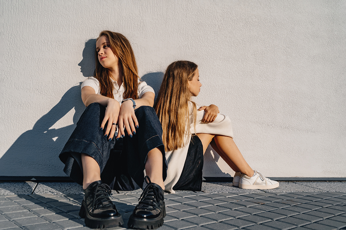 Two girls sitting by a wall facing away from each other