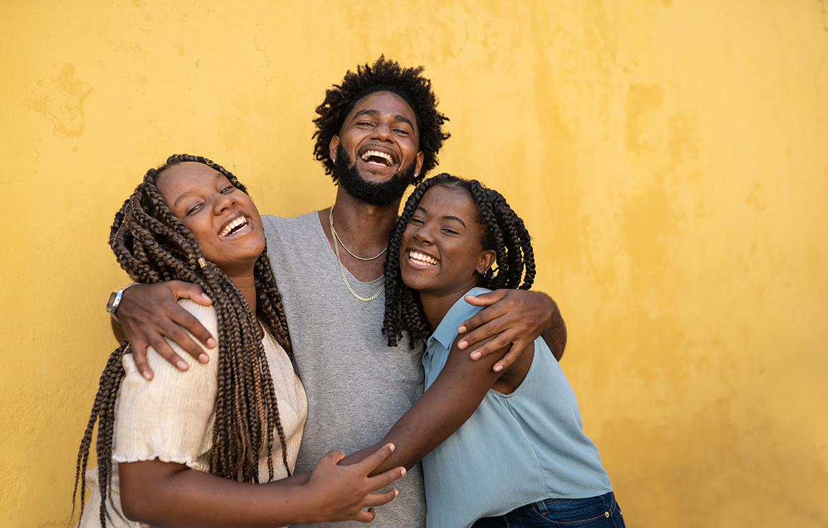 Two women and a man hugging against a yellow background