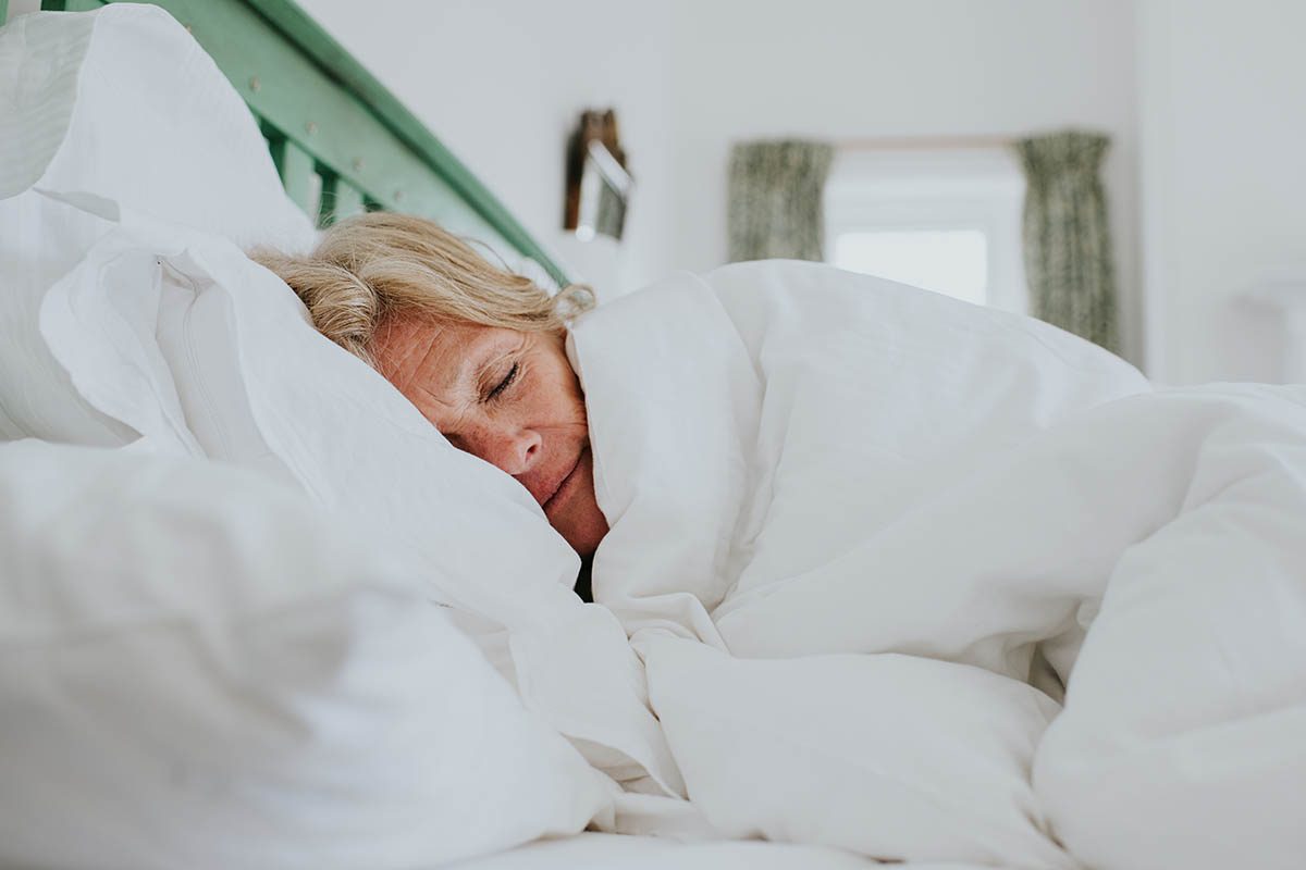 A sleeping woman is wrapped in a thick, white duvet in a double bed.