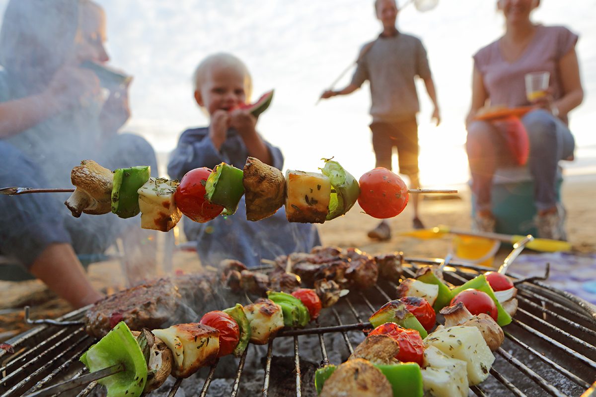 A family cooking kebabs on a barbecue at the beach