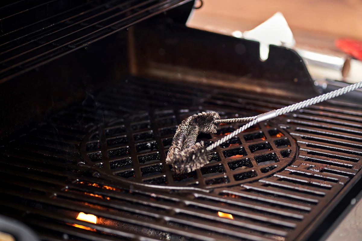 A close-up of someone cleaning a barbecue with a brush