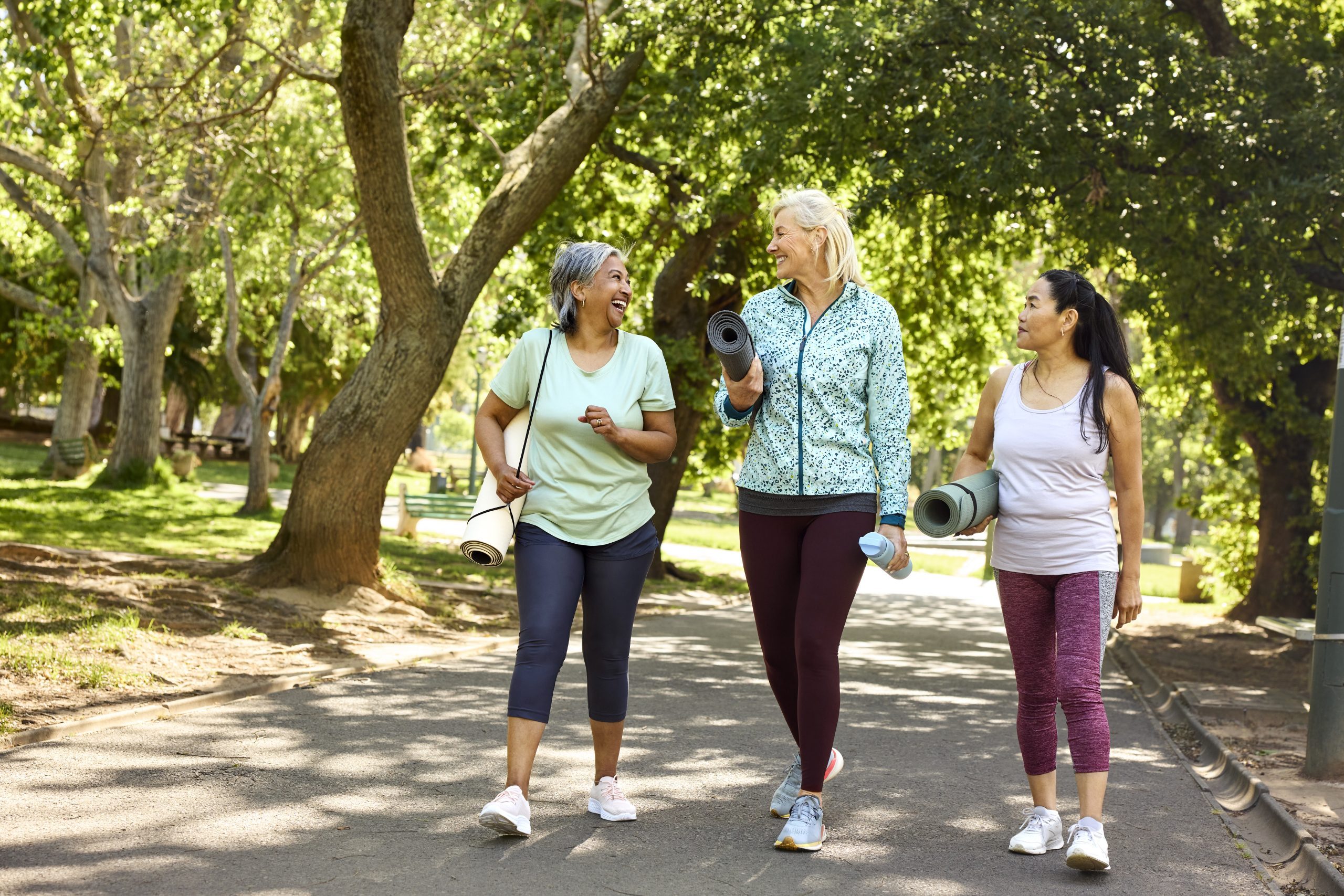 Three women carrying yoga mats are walking in a park