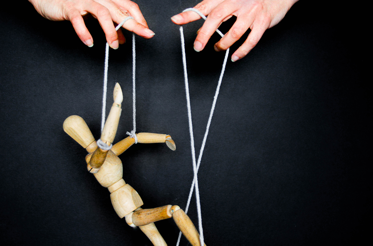 Hands moving a wooden mannequin with strings