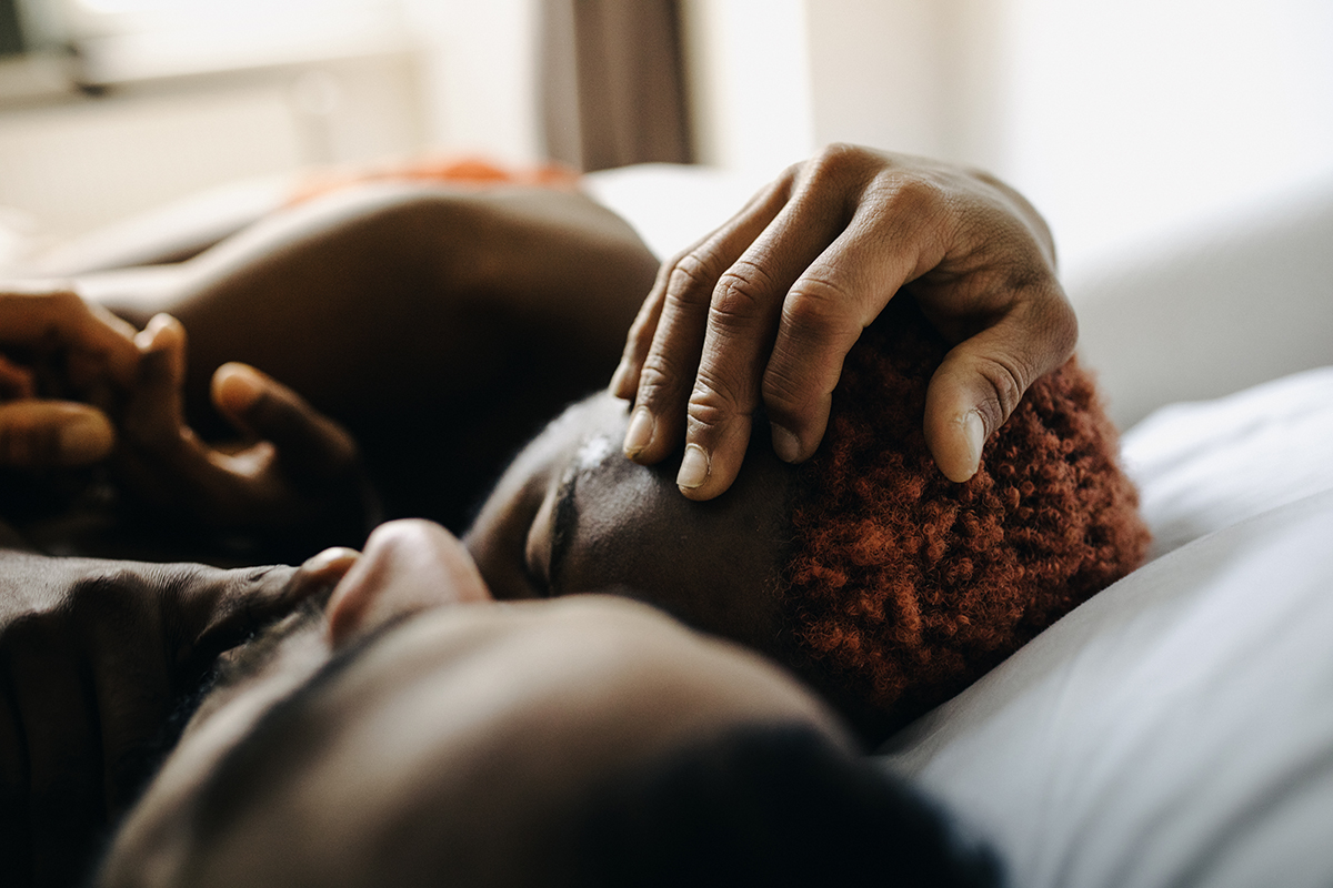 A man stroking another man's head in bed